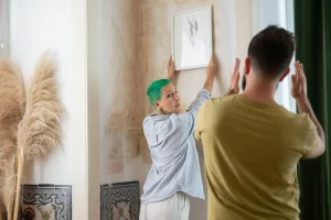A couple collaborates to hang artwork in a stylishly decorated room, enhancing their home design.