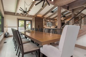 Long dining table with slat-back chairs and white host chairs under starburst chandeliers