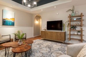 Media room with a TV on a wood credenza, ladder shelving and coastal art