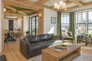 Open living room with a leather sofa and green drapes under timber beams