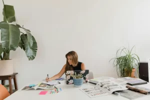 Contemporary home office setup featuring a woman working amidst lush houseplants and design magazines.