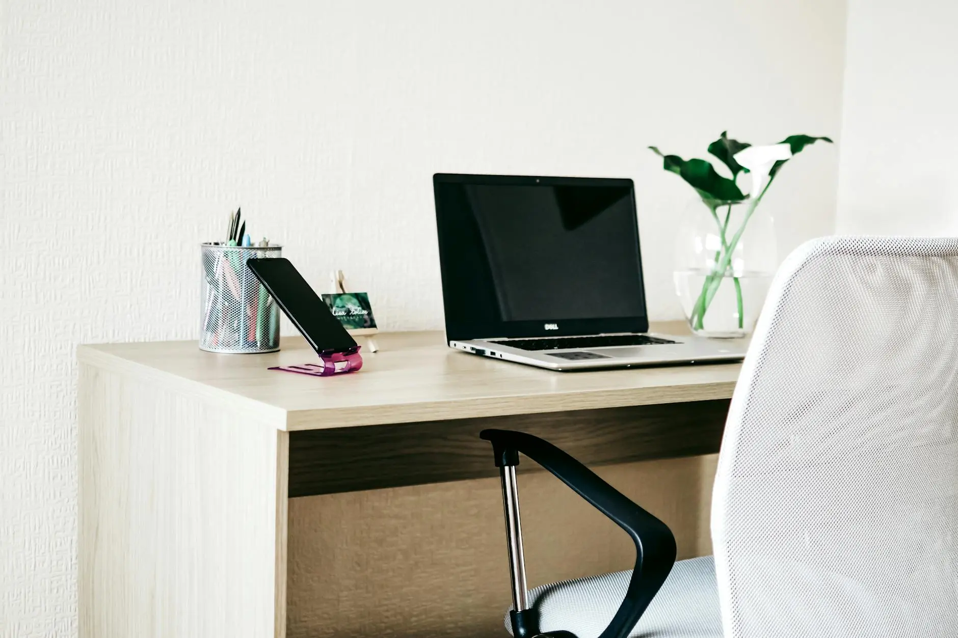 A clean and modern home office workspace with a laptop, smartphone, and plant on a wooden desk.