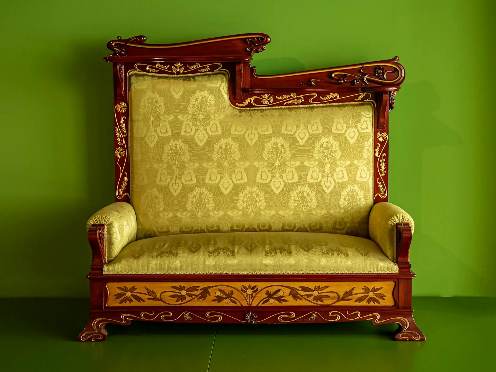 A beautifully ornamented vintage sofa with intricate designs against a vivid green backdrop.
