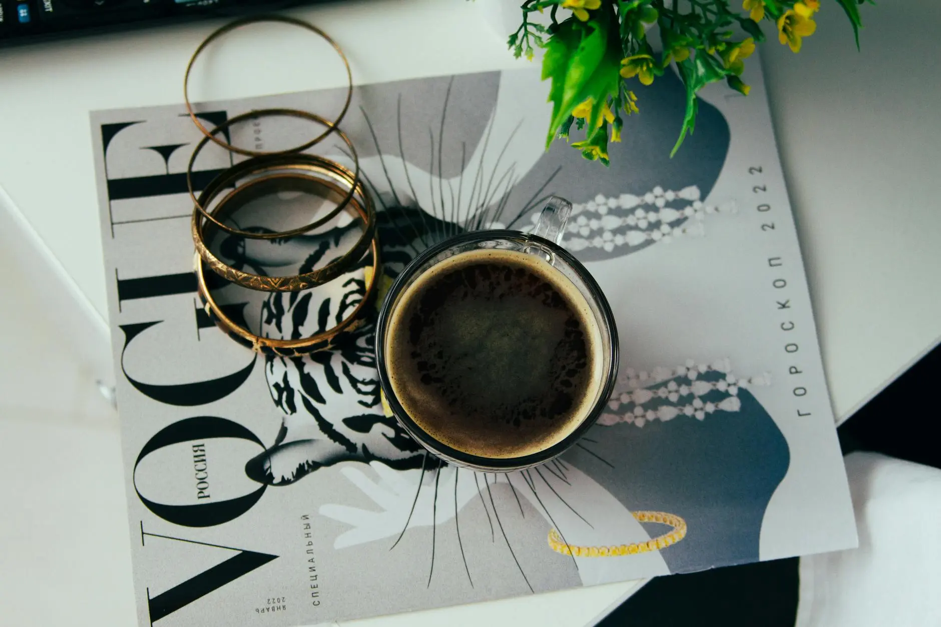 Flat lay of coffee on magazine with bangles, featuring modern aesthetic.