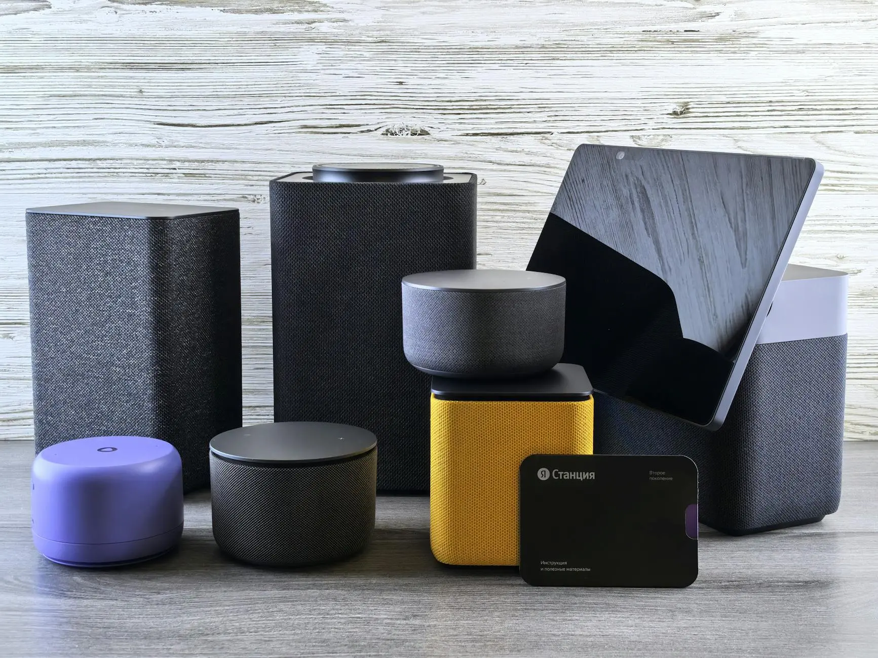 A collection of various smart home speakers and tablet displayed on a wooden surface.